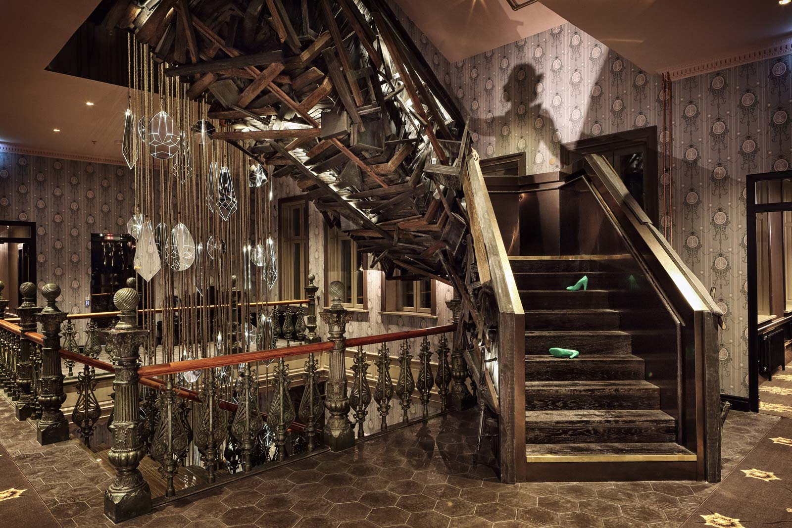 Trappa med unik träkonstruktion och hängande glaskonstverk i en sofistikerad hotellfoajé med vintage inredning.