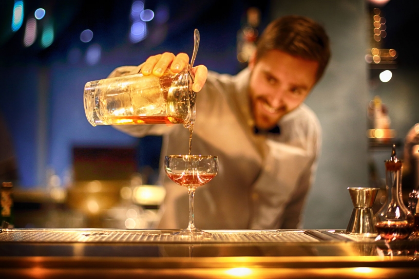 Glad bartender häller upp ett glas vin vid en bar med suddig bakgrund.